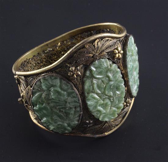 A Chinese silver gilt filigree bracelet inset with three carved jadeite oval foliate panels.